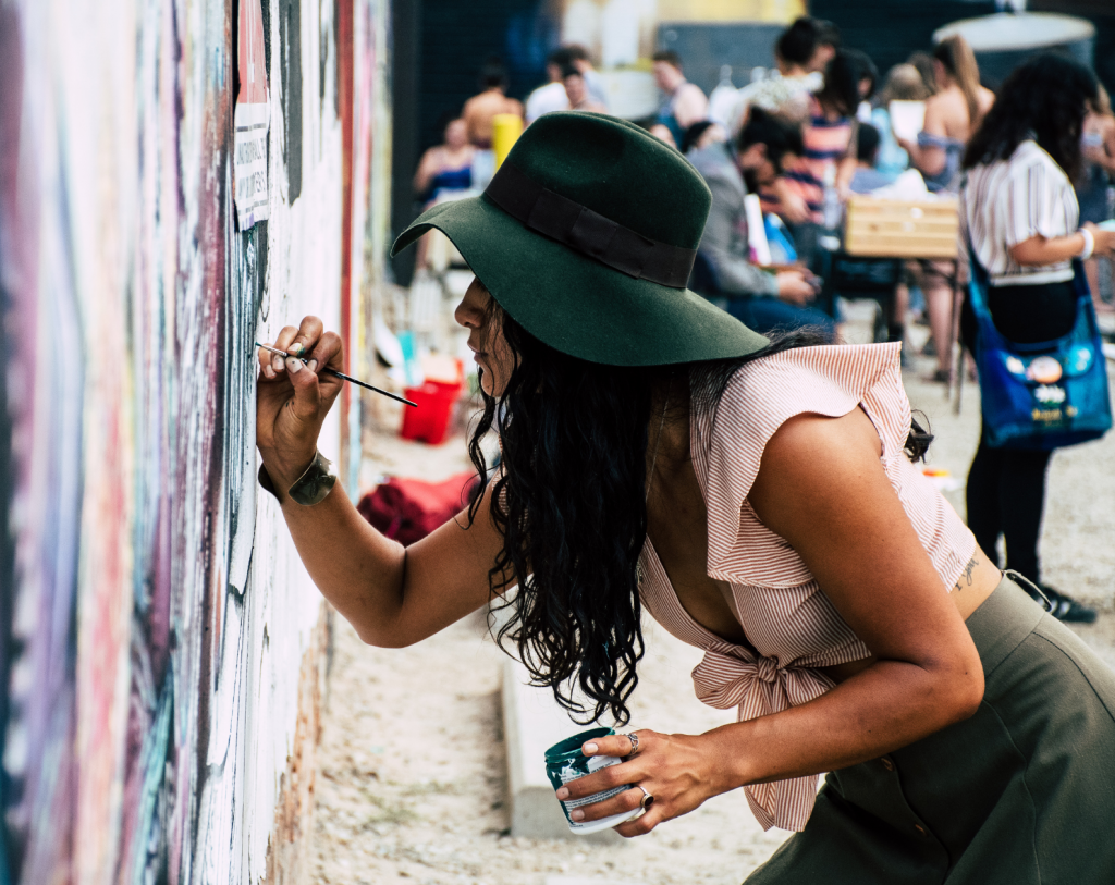 A woman in a felt hat is concentrating and painting a mural.
