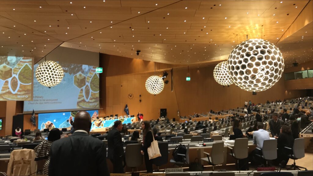 A large conference room. Delegates of the WIPO Diplomatic Conference are taking their seats.