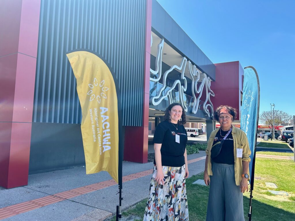 Two women standing in front of a large building with colourful flags out front.