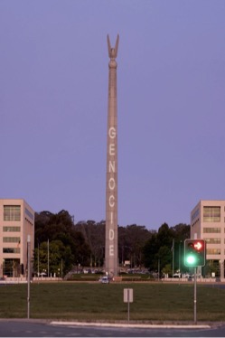 Image of a large public structure with the word 'genocide' projected on it.